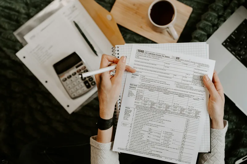 Person reviewing paperwork with a calculator and laptop at a desk