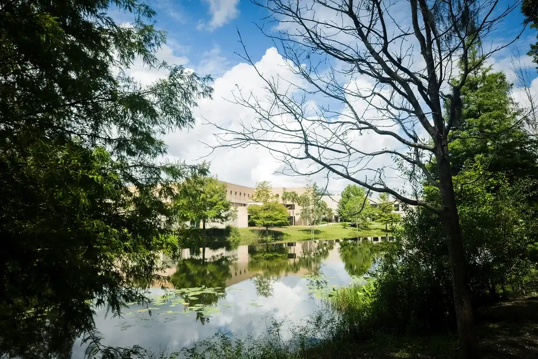 Low office buildings reflected in a calm pond, framed by trees