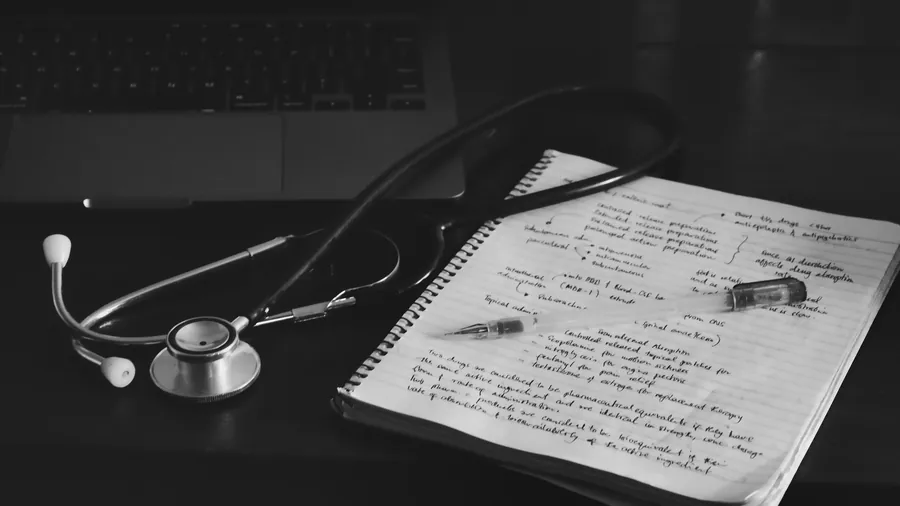 A stethoscope beside a handwritten notebook and a laptop